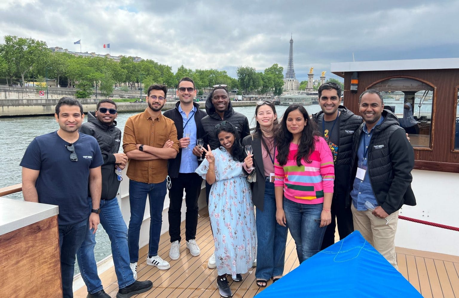 Anish Pahwa & Shikhar Jamuar with a group of people beside a Paris river with the Eiffel tower in the background.